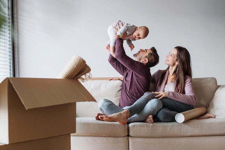 Happy family in new home with moving box, celebrating real estate purchase after their agent introduced them to a cost-effective alternative to traditional title insurance via AOLPro.