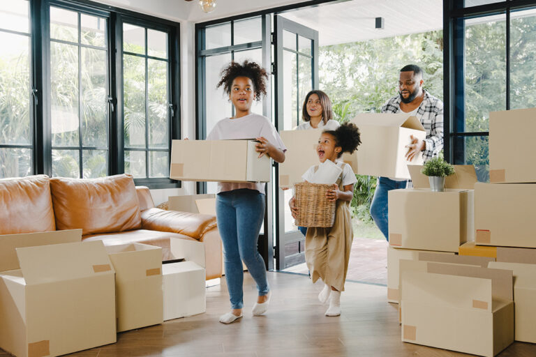 Young family of four holding boxes and moving into new home, happy because their lender used AOLPro and they saved money this alternative to traditional title insurance.