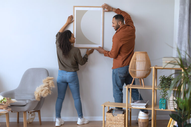 Young couple hanging art in new home, happy because they discovered a cost-effective alternative to traditional title insurance called AOLPro.
