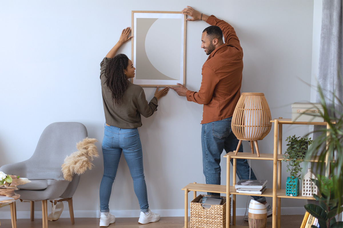 Young couple hanging art in new home, happy because they discovered a cost-effective alternative to traditional title insurance called AOLPro.